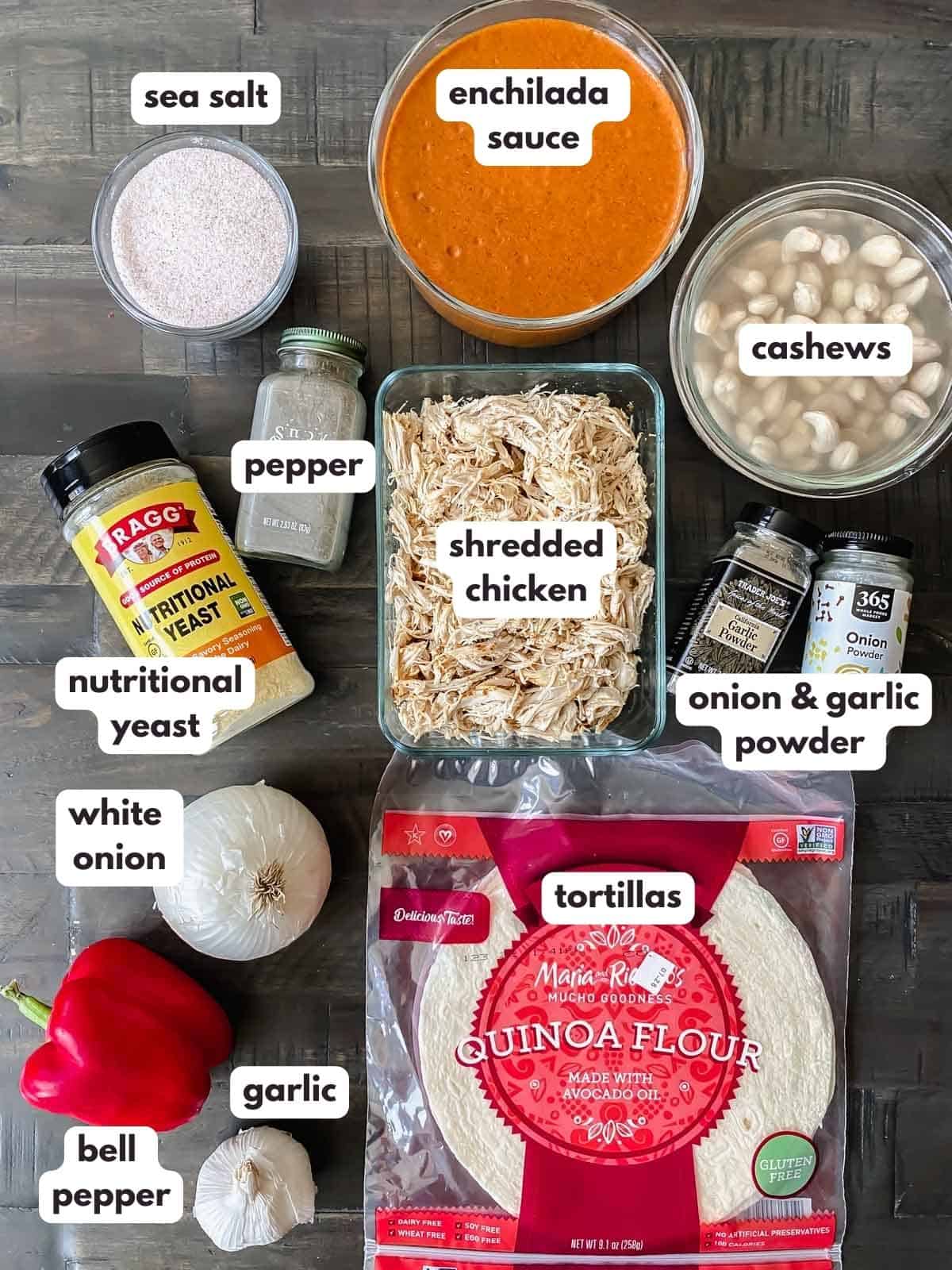 labeled enchilada ingredients on table - bell pepper, garlic, tortillas, white onion, enchilada sauce, shredded chicken, nutritional yeast, sea salt, pepper, onion and garlic powder, cashews.