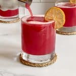 hibiscus vodka cocktail being poured into short glass from cocktail shaker.