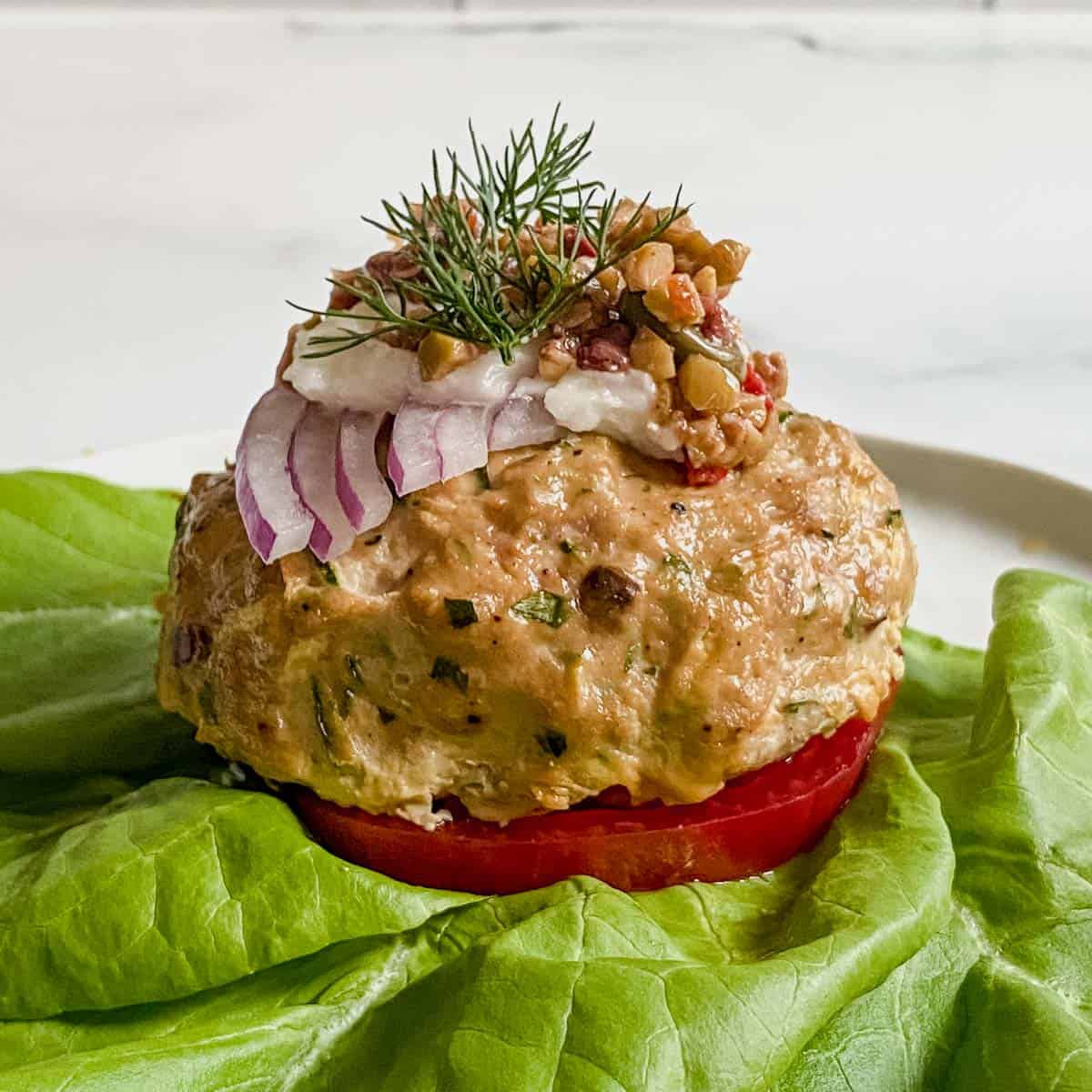 Turkey burger on lettuce wrap with slice of tomato and topped with olive tapenade.