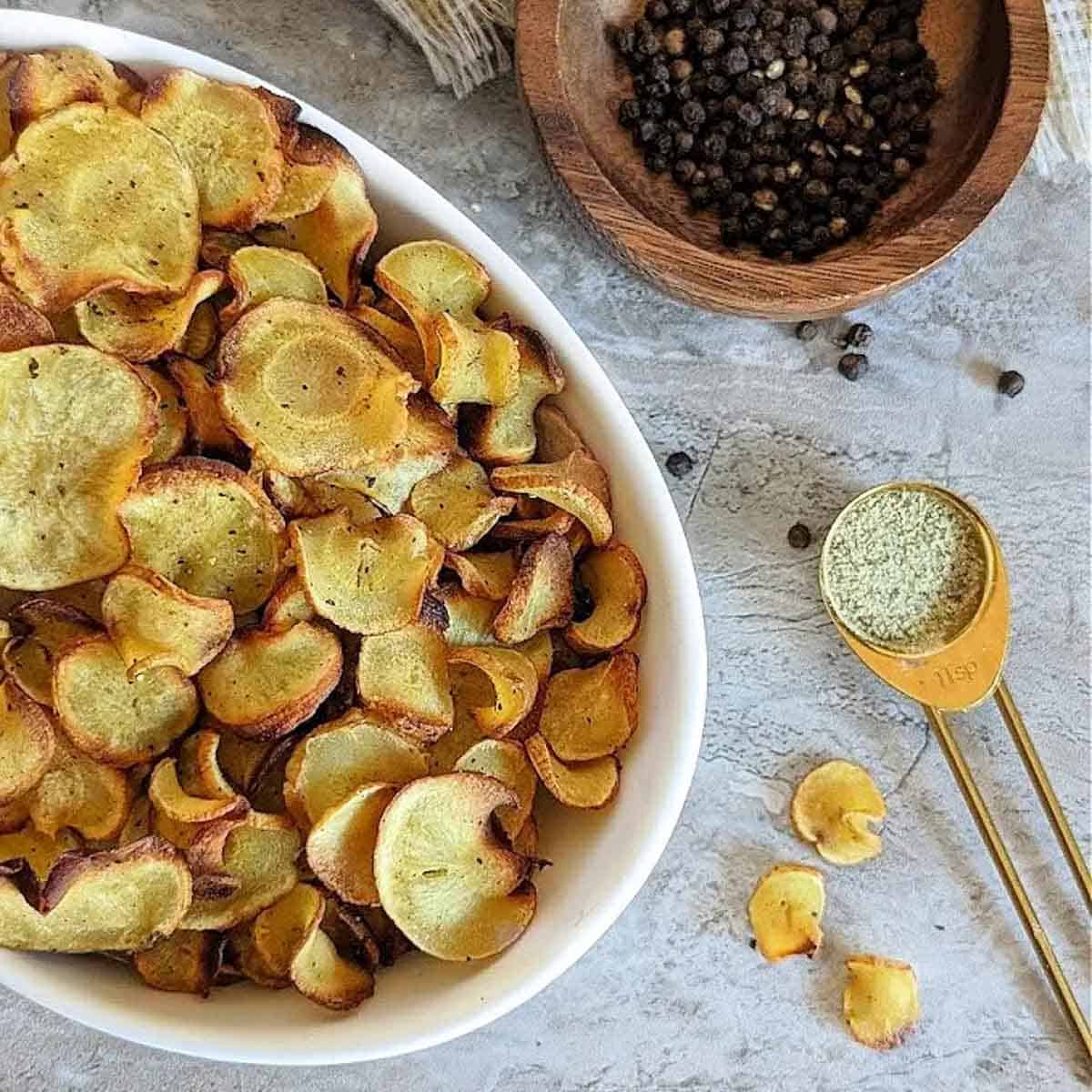 parsnip chips on oval bowl next to seasonings on table.