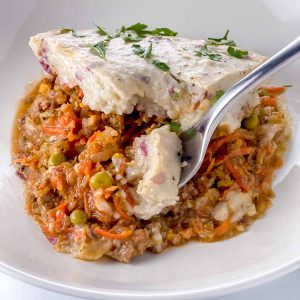 cottage pie on a white plate with a fork taking a scoop out of it.