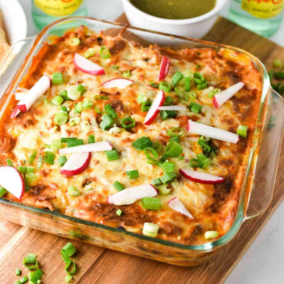 enchilada casserole in glass baking dish topped with sliced scallions and radishes.