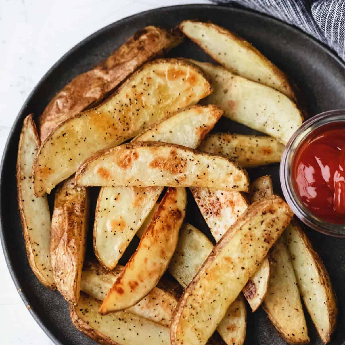 roasted potato wedges on a black plate with ketchup.
