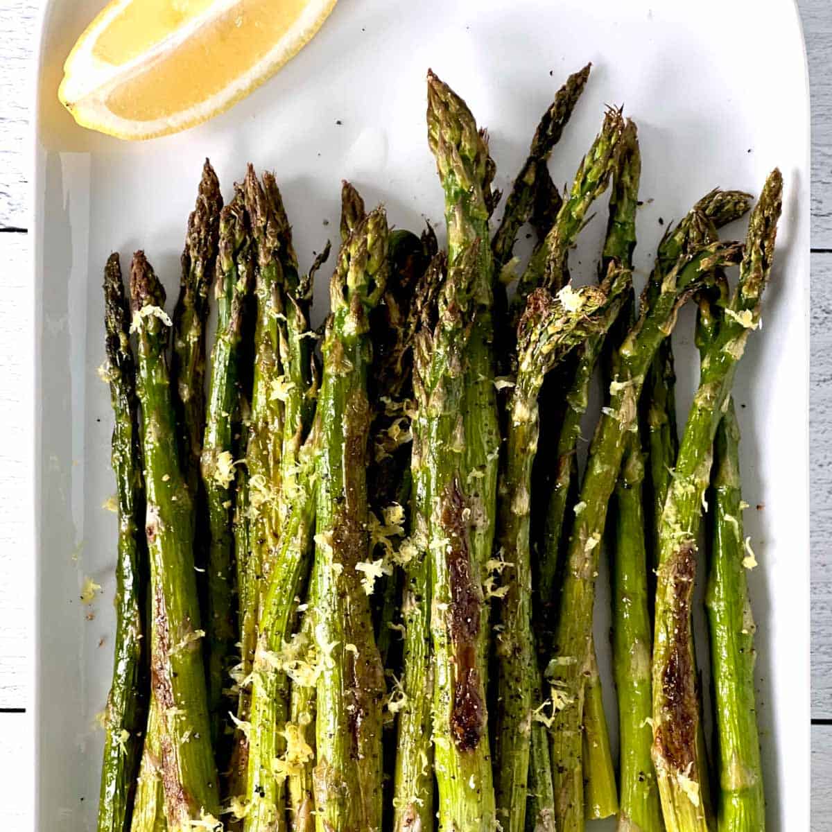 roasted asparagus on a white tray with lemon wedge.