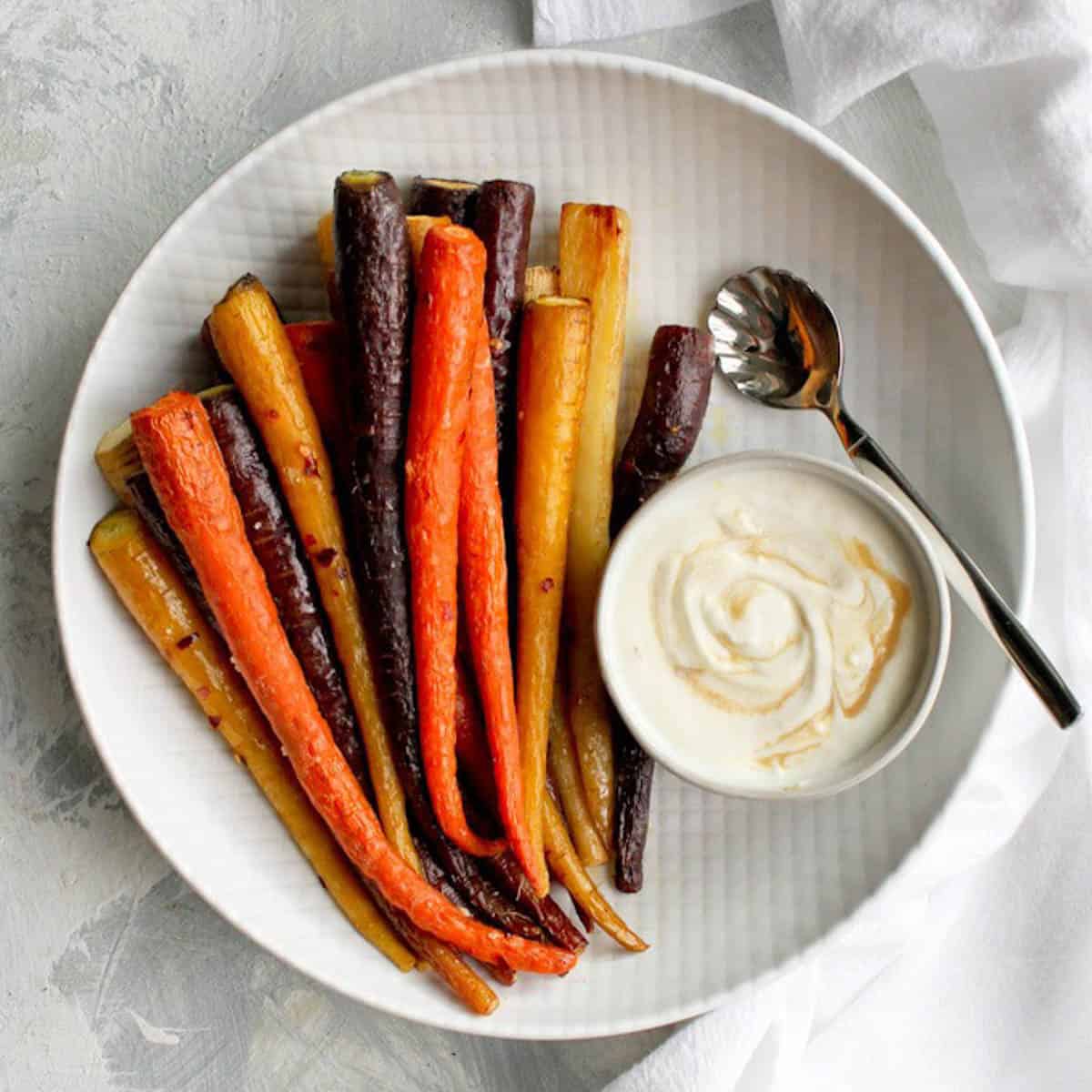 roasted colorful carrots on large white tray next to tahini sauce in small bowl on the tray.
