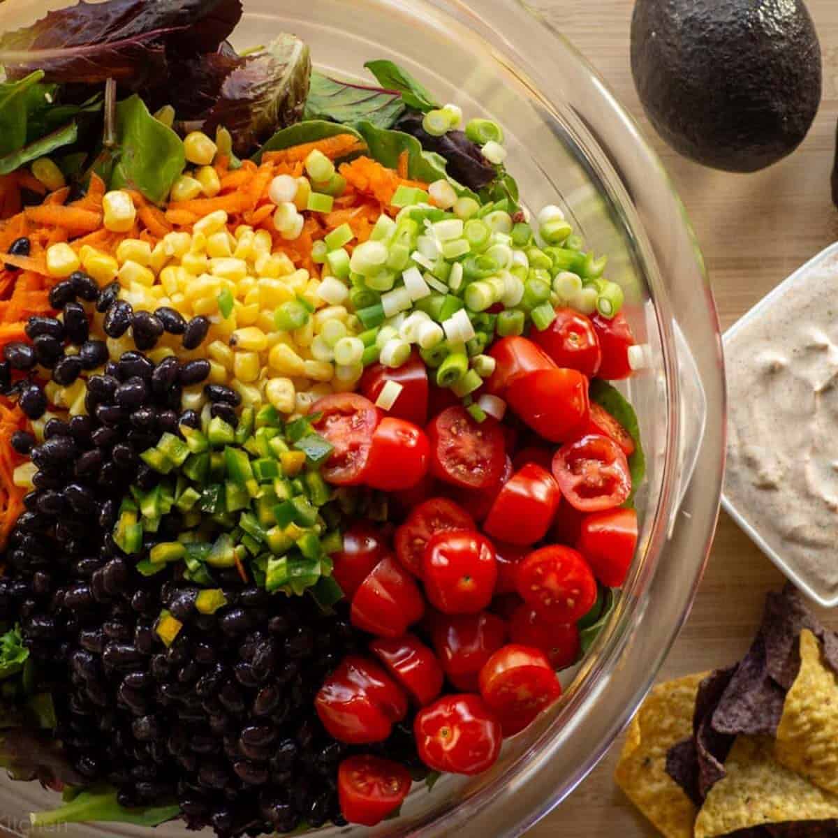 veggies in salad bowl next to some tortilla chips and small bowl of ranch.