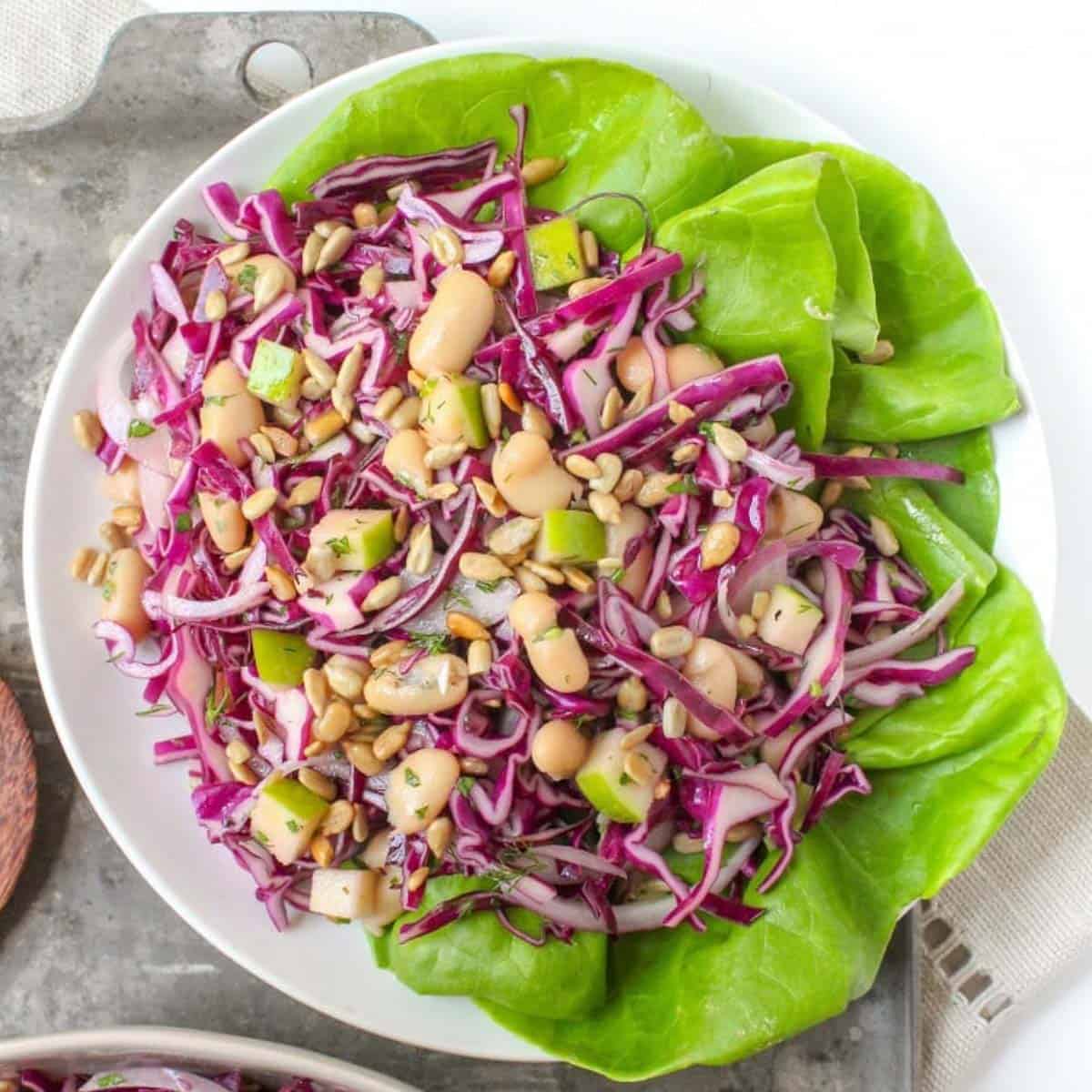 white bean apple cabbage slaw on an oval plate over some large lettuce leaves.