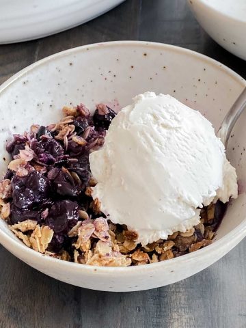 healthy blueberry crumble in a small bowl with dairy free ice cream.