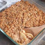 healthy apple crisp in a glass baking dish with wooden spoon taking a spoonful.
