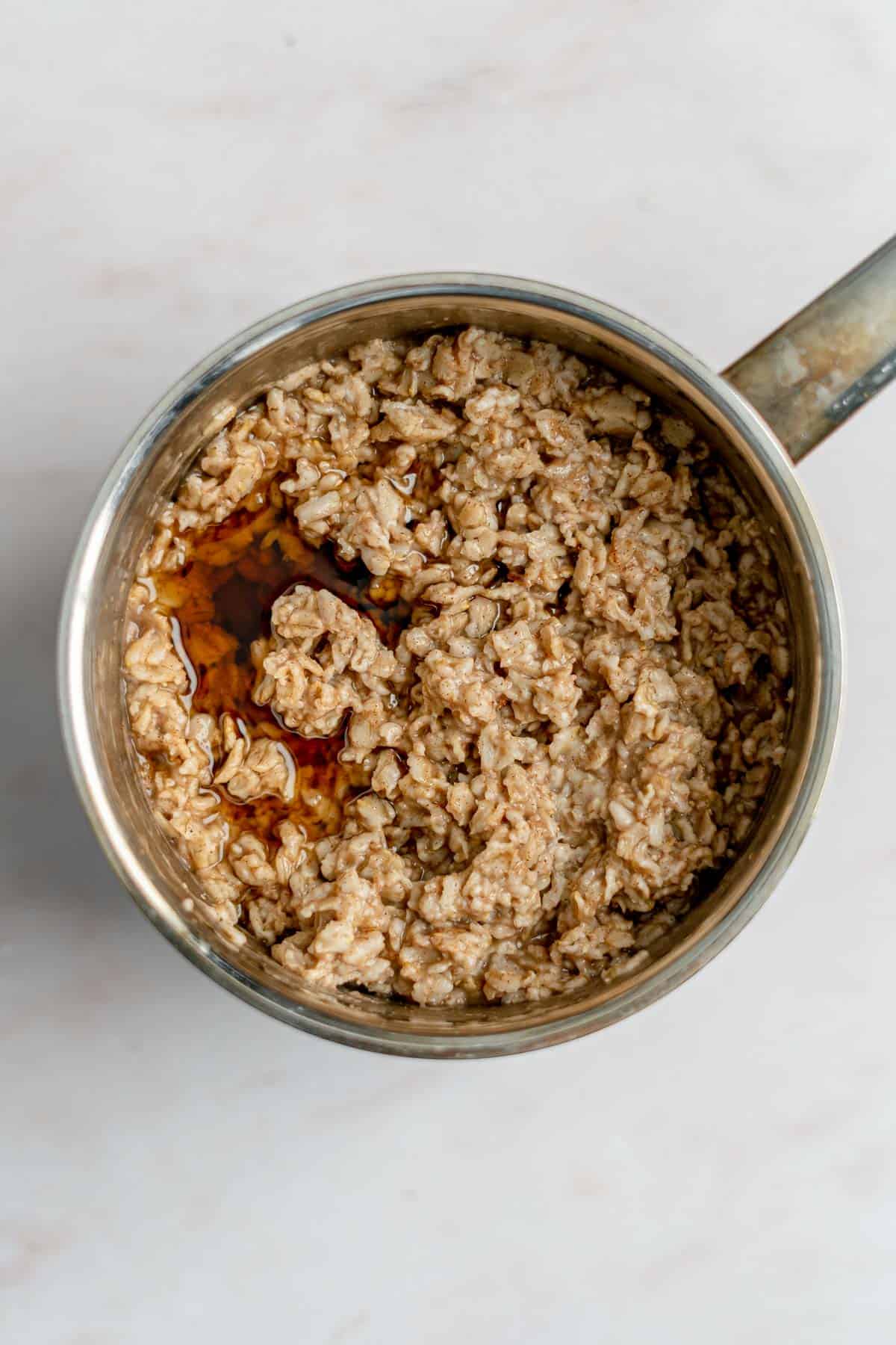 cooked oatmeal in pot with maple syrup on top.