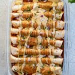 Enchiladas after being baked in the pan with extra dairy free cheese sauce, diced red onion and shredded cilantro on top.