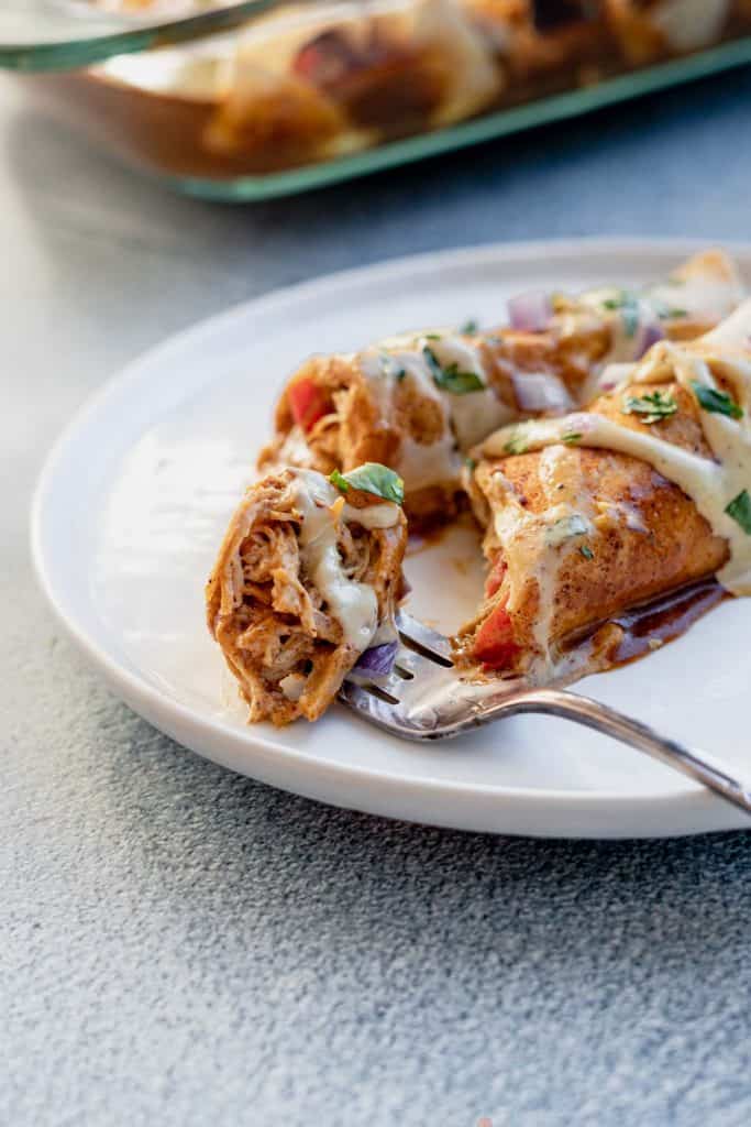 An enchilada cut in half on plate with fork taking a bite.