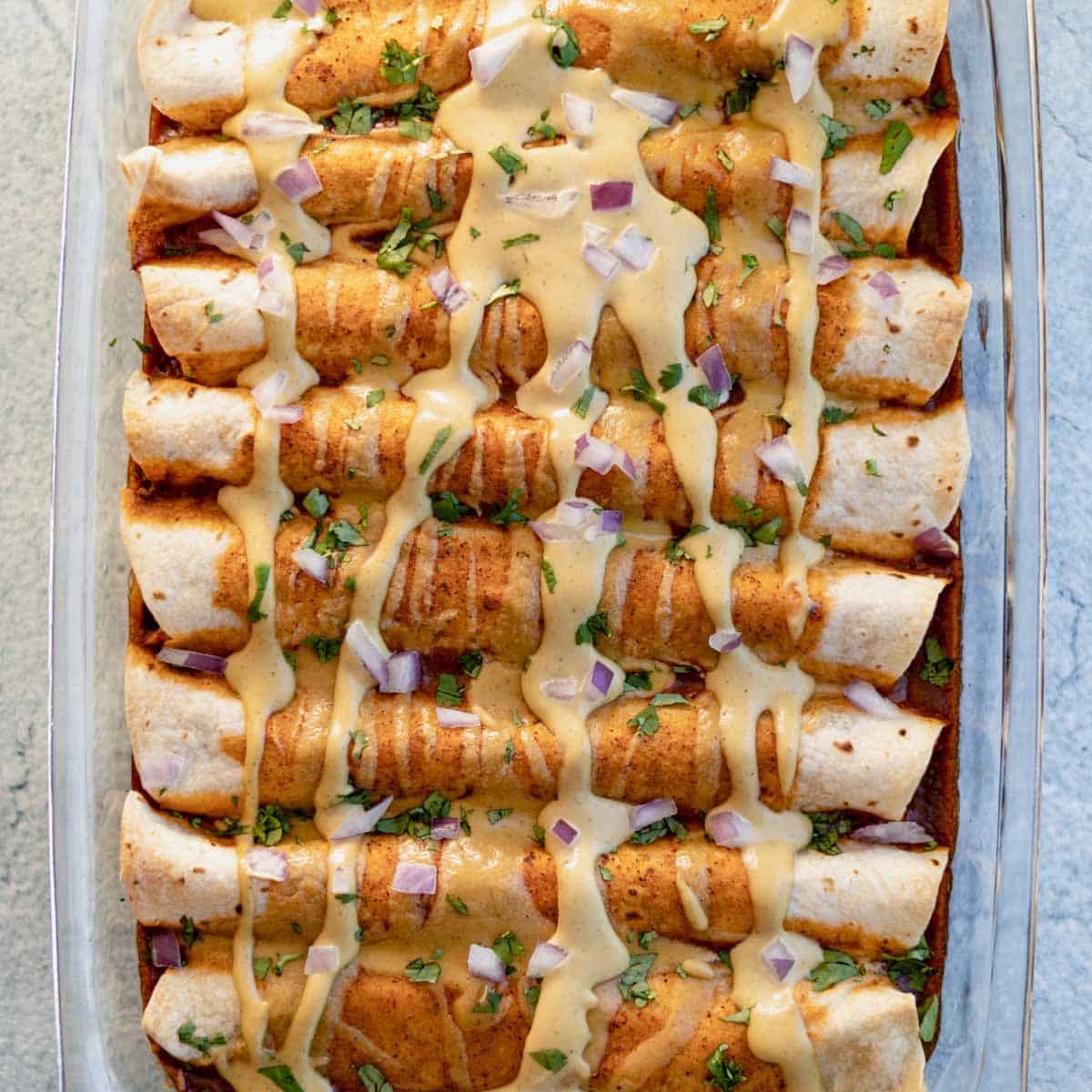 Pan of enchiladas with homemade dairy free cheese sauce on top.