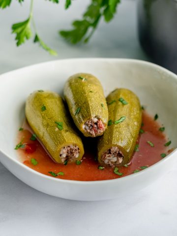 3 stuffed squashes stacked in pyramid in large bowl with tomato brine on the bottom.