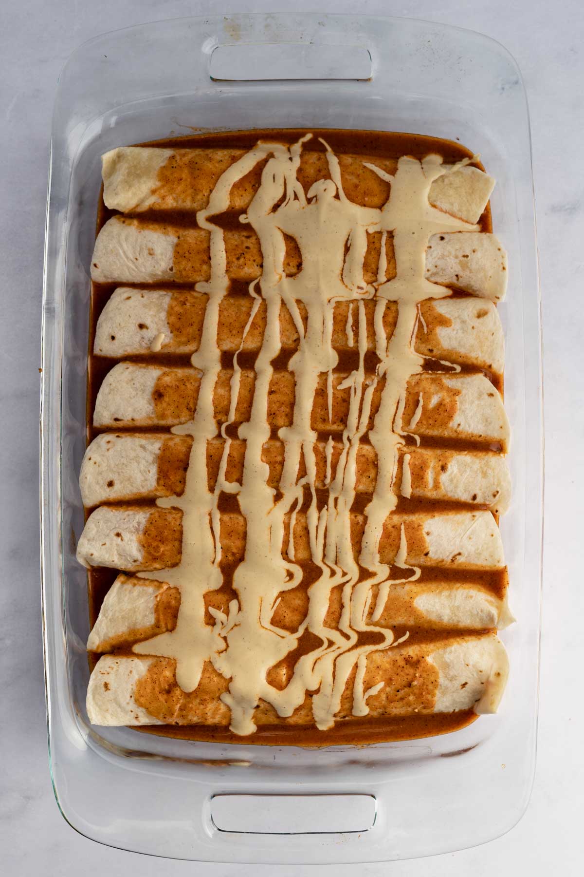 8 enchiladas in a pan with enchilada sauce and cheese sauce poured on top being before baked.