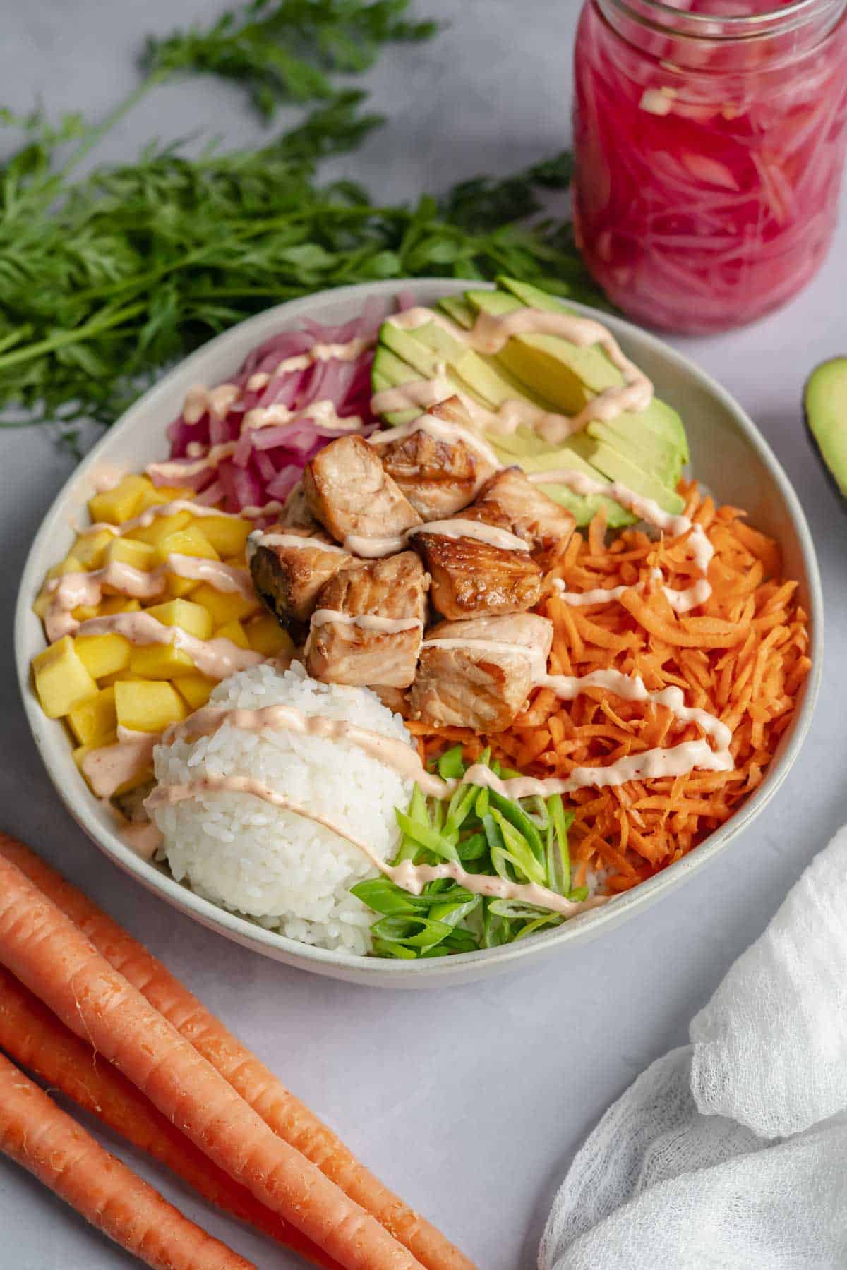 cooked salmon poke bowl assembled in white bowl with spicy mayo drizzled on top.