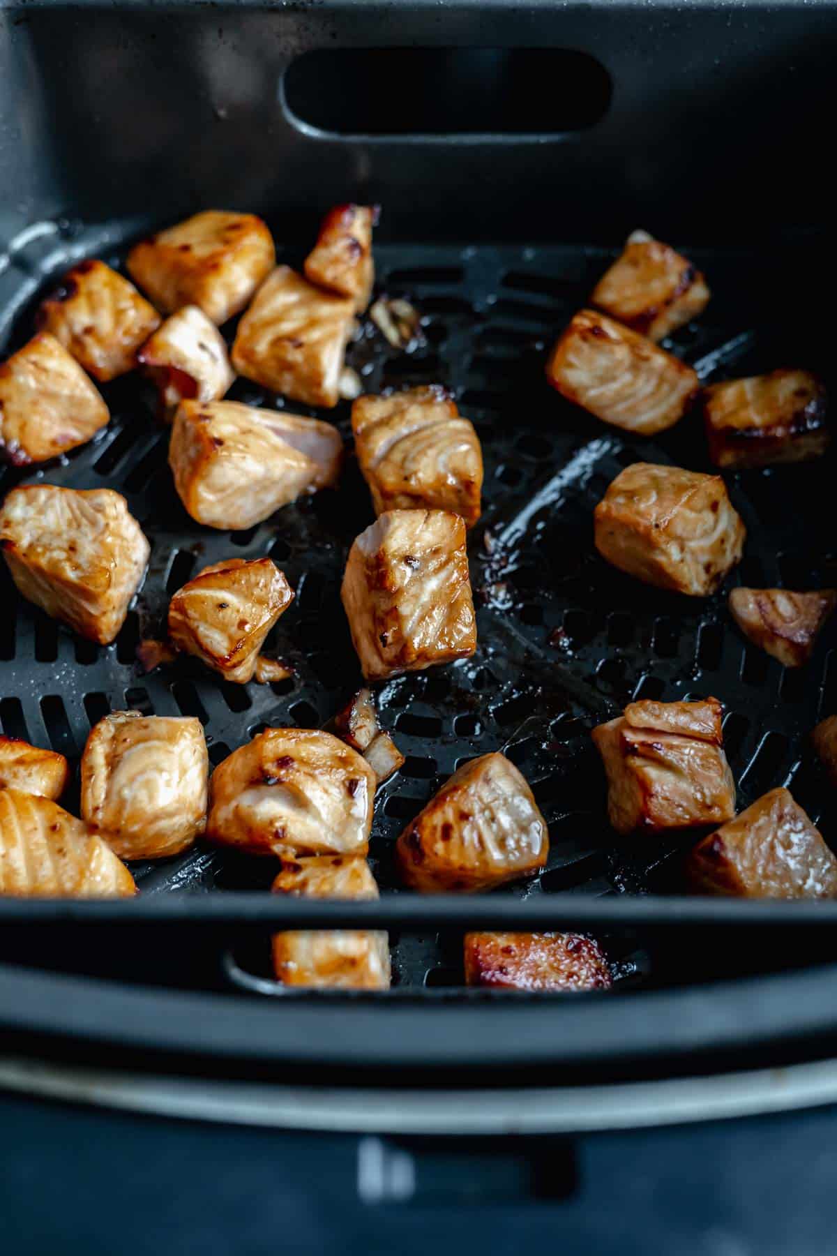 salmon being cooked in air fryer basket.
