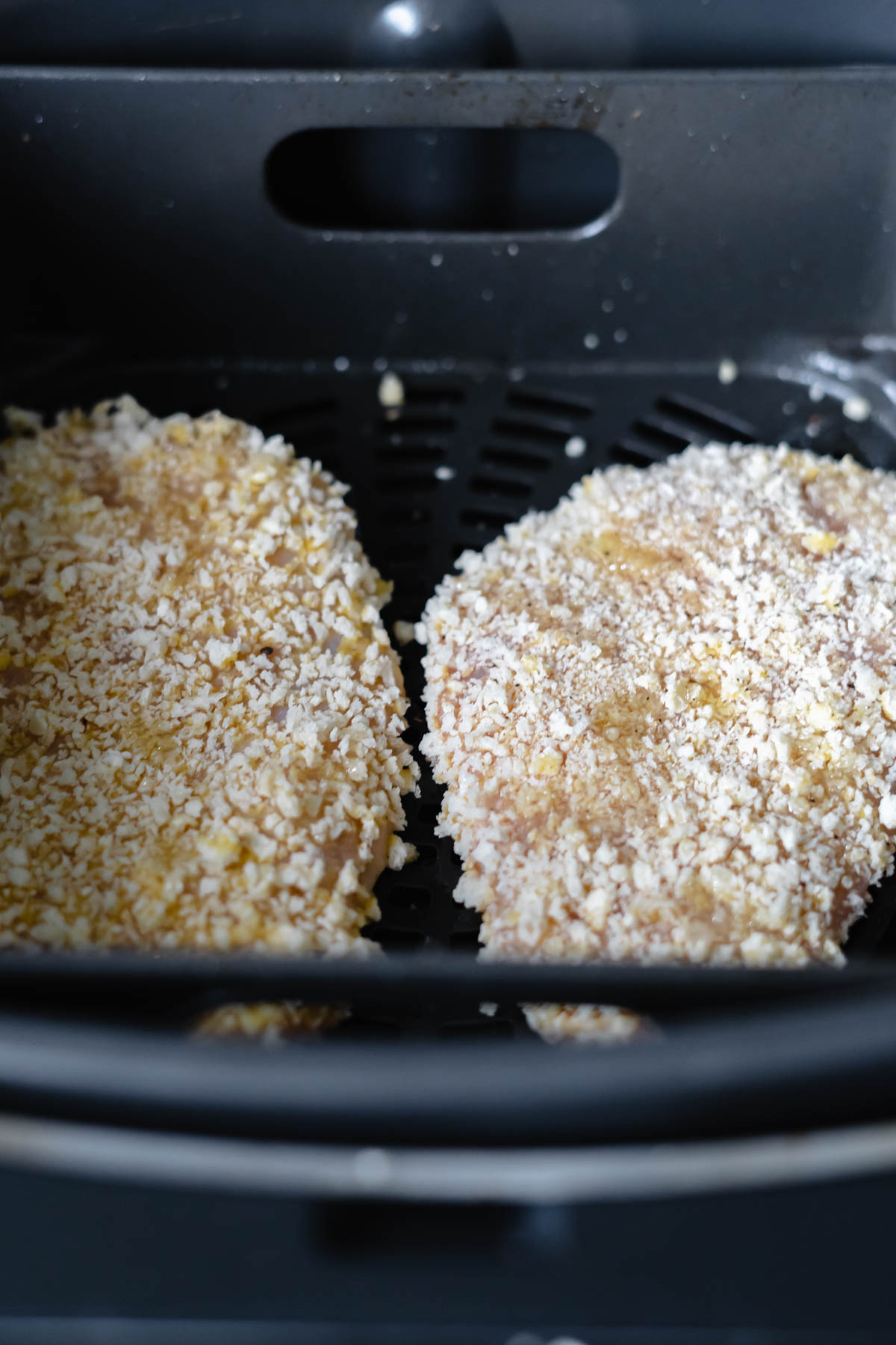 two pieces of uncooked breaded chicken in air fryer before being cooked