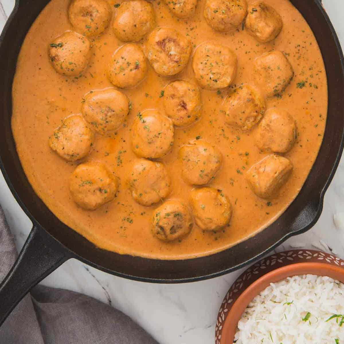 butter chicken meatballs in skillet with sauce and a small bowl of rice on the side.