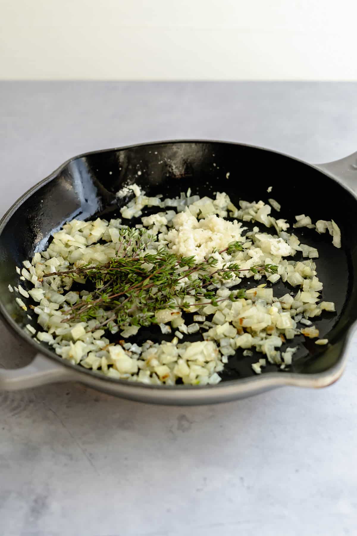 onion, garlic and thyme sprigs being sautéd in pan.