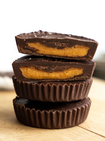 close up of peanut butter cups stacked with top one cut in half with insides showing.